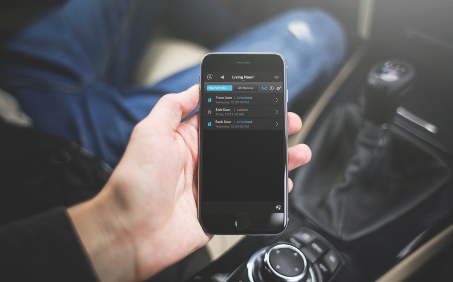  A man holding a smartphone in a car that shows the status of various parts of his home’s security system. 