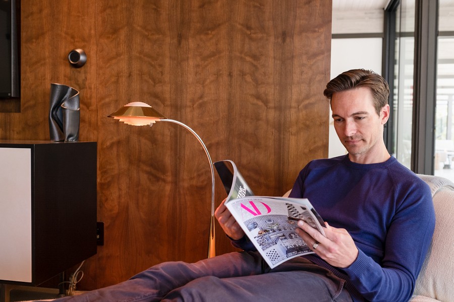 A man reads a magazine on a chaise; a wall-mounted  Josh.ai voice control microphone is in the background. 