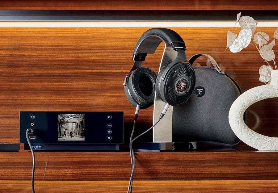 A Focal Utopia headphone is hung on a stand next to a music streaming amplifier.
